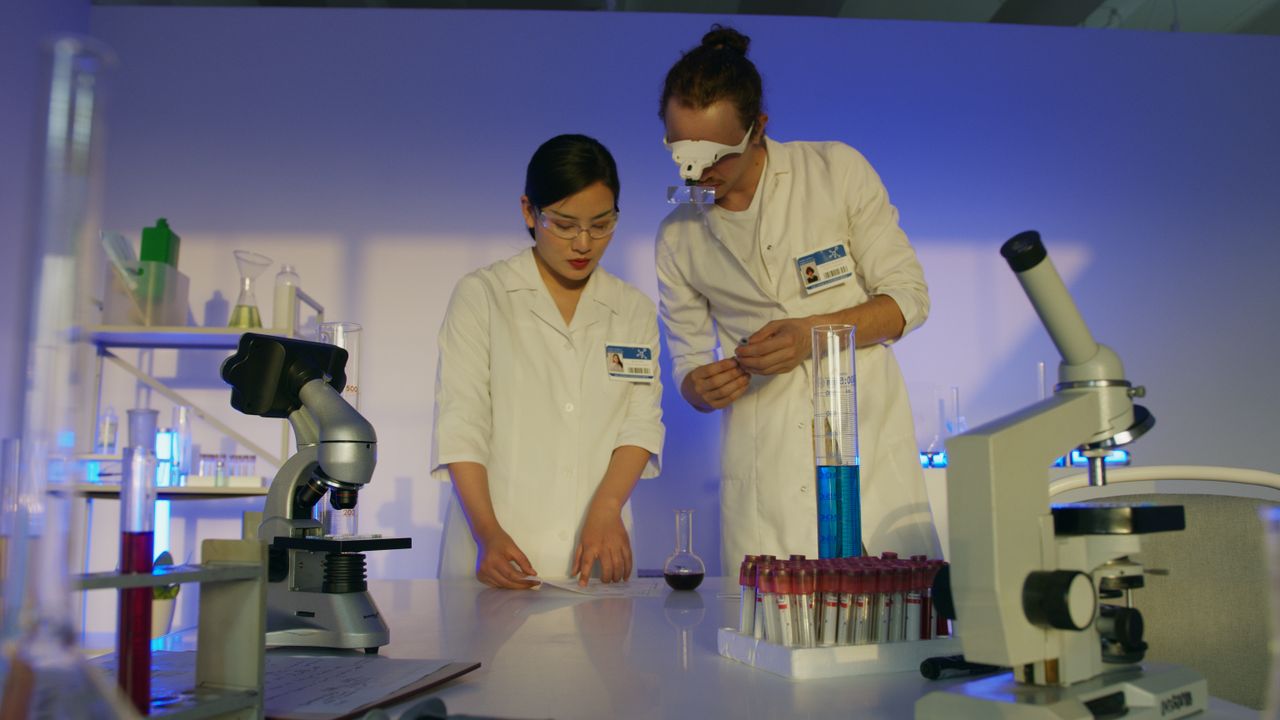 Two scientists in a lab conducting experiments with microscopes and test tubes.